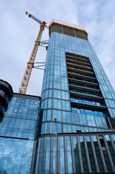 A towering skyscraper under construction with a prominent industrial crane against a blue sky.
