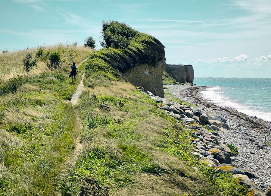 Scenic coastal path along cliffs in Rødby Sogn, Denmark, with a lone hiker.
