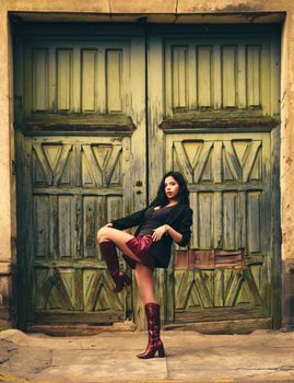 Young woman in fashionable outfit poses confidently in front of vintage wooden doors.