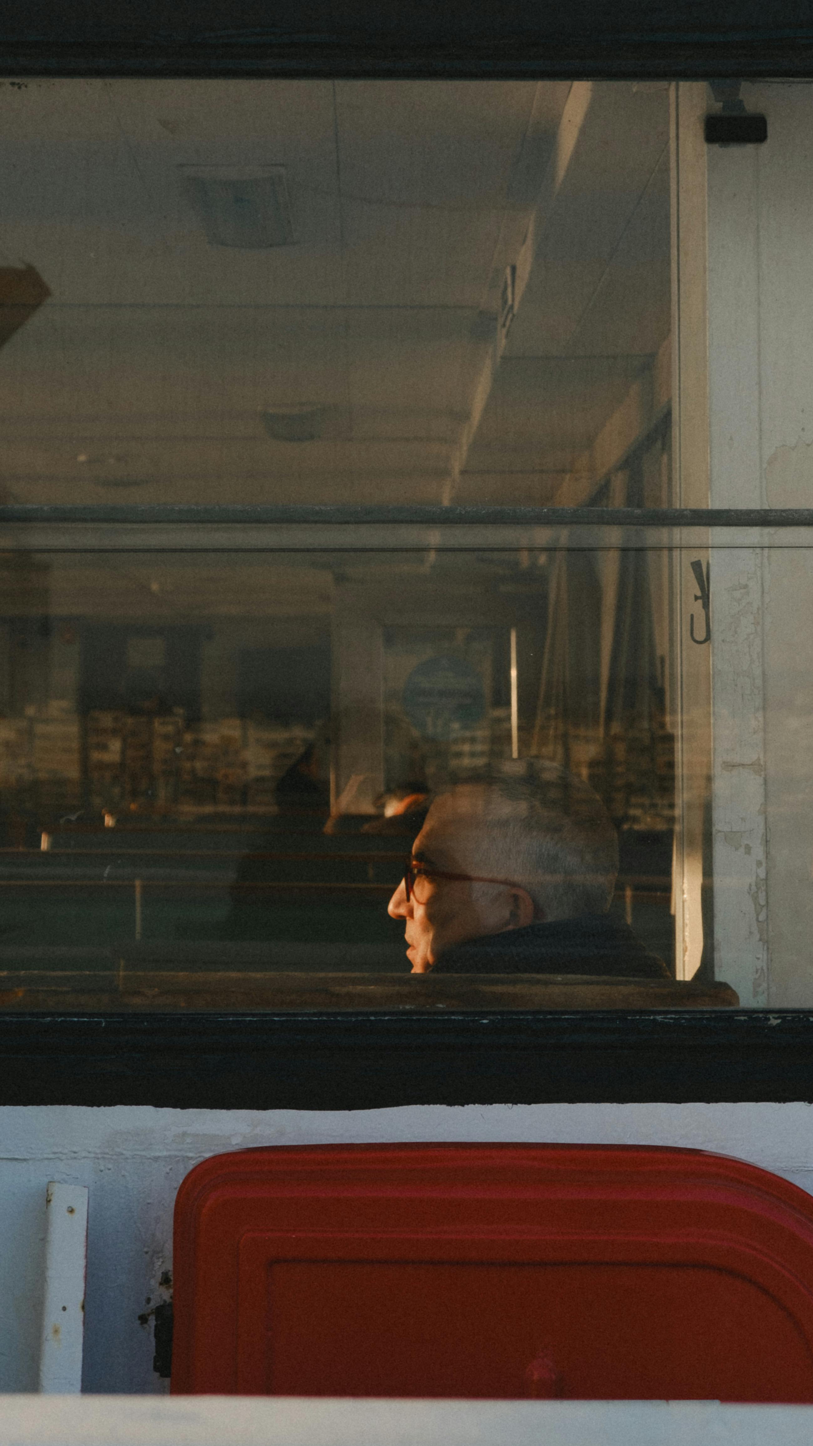 grátis Um senhor idoso sentado sozinho, olhando pela janela da balsa com uma expressão contemplativa. Foto profissional