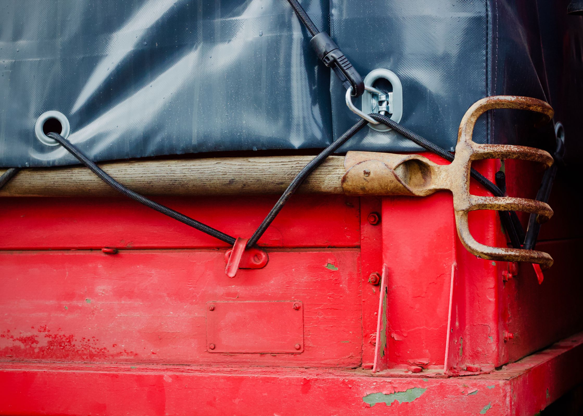 Black bungee cord hooked to a red truck bed holding down a tarp