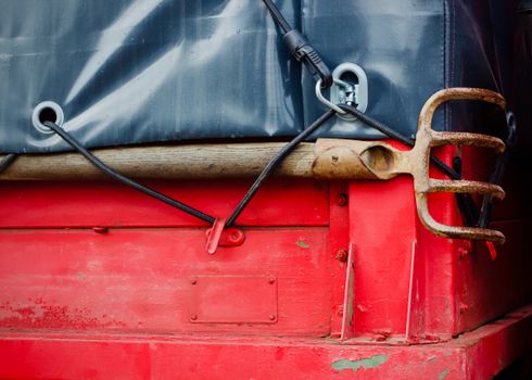 Rusty pitchfork and bungee cords on a vibrant red truck surface.