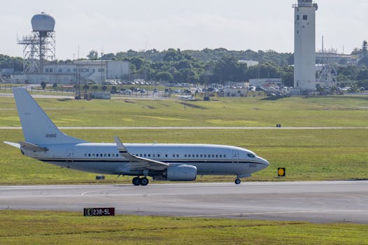 Commercial airplane taxiing on airport runway with control tower background in daylight.