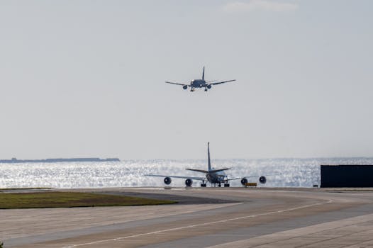 Two airplanes on a sunny runway by the sea, one landing and the other on ground.