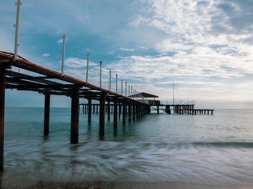 Free A serene pier stretching into the ocean under a cloudy sunrise sky, ideal for relaxation. Stock Photo