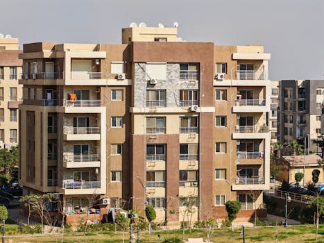 A sunny urban scene of a modern apartment building exterior with balconies and greenery.