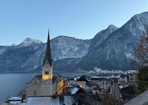 Breathtaking winter view of Hallstatt village with snow-capped mountains and lakeside church.