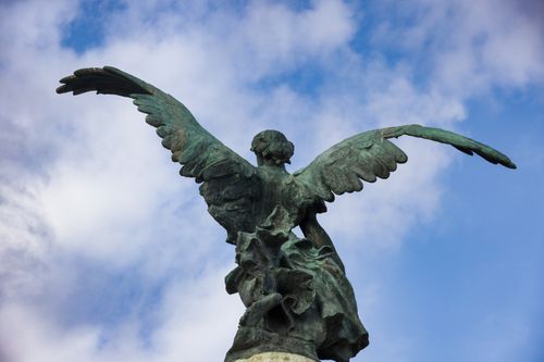 Free Sculpture of an angel with wings open against a sky backdrop. Stock Photo