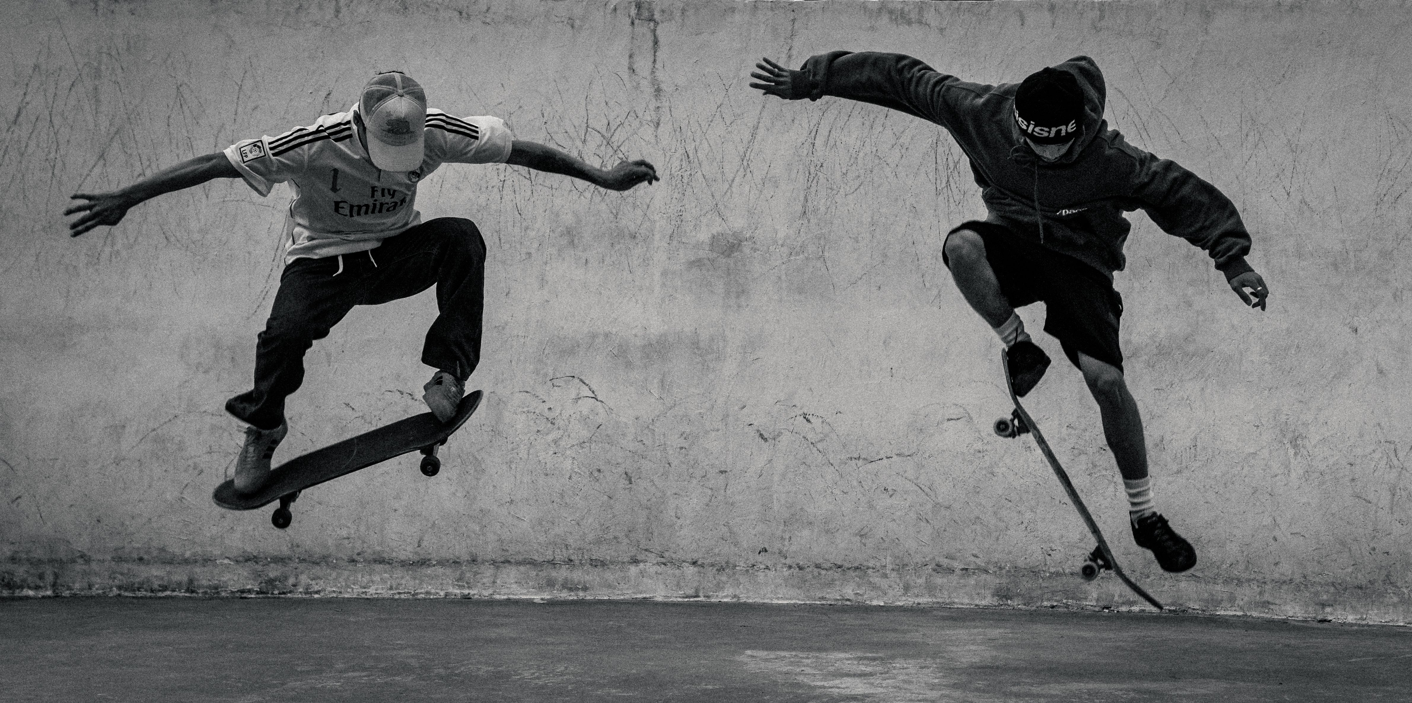 Two skaters executing tricks indoors, captured in high contrast black and white.
