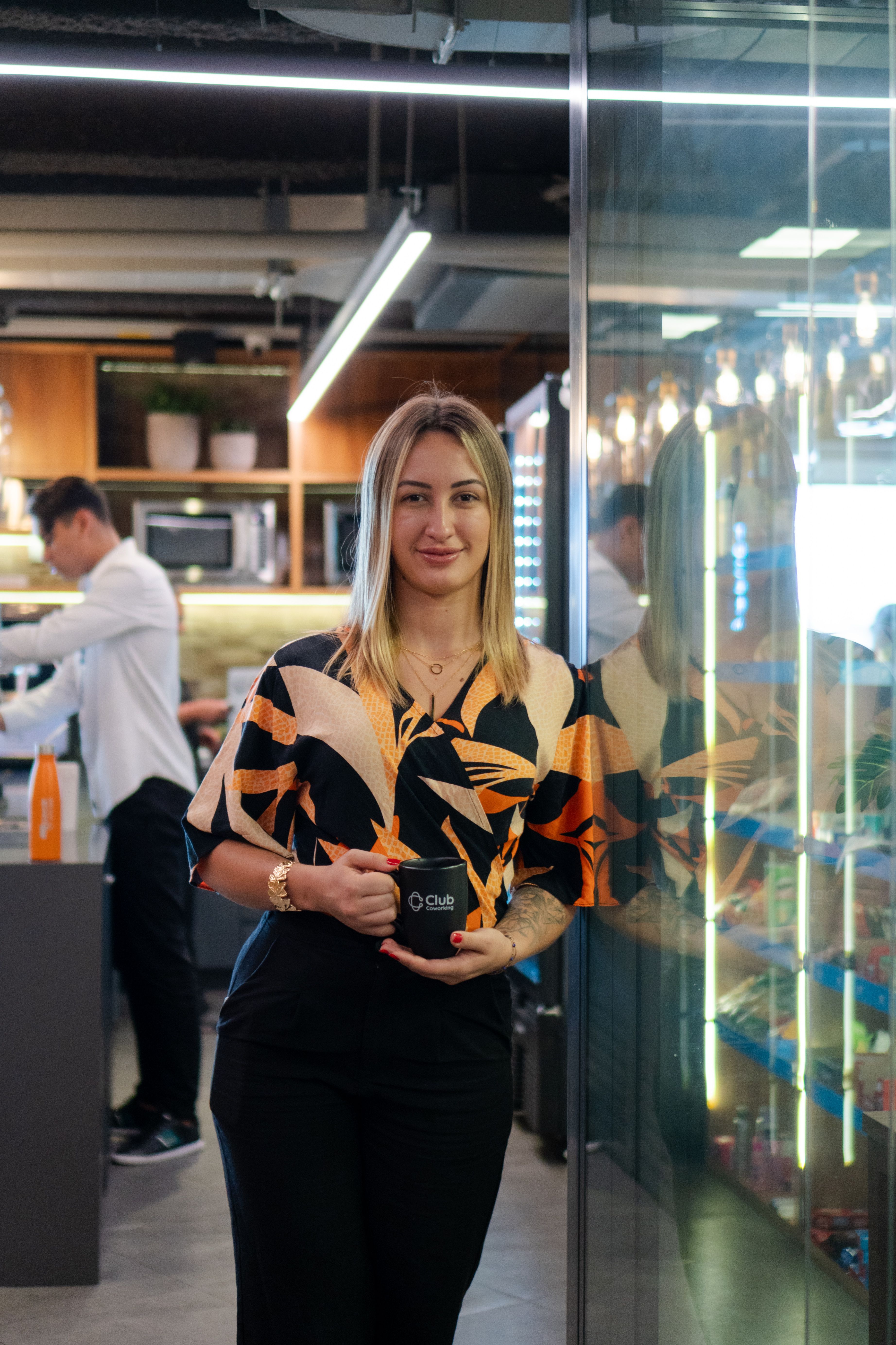 A confident woman stands in a modern office environment holding a coffee cup.