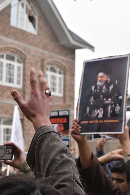 Protesters raise hands holding a Khamenei poster, expressing dissent outdoors.