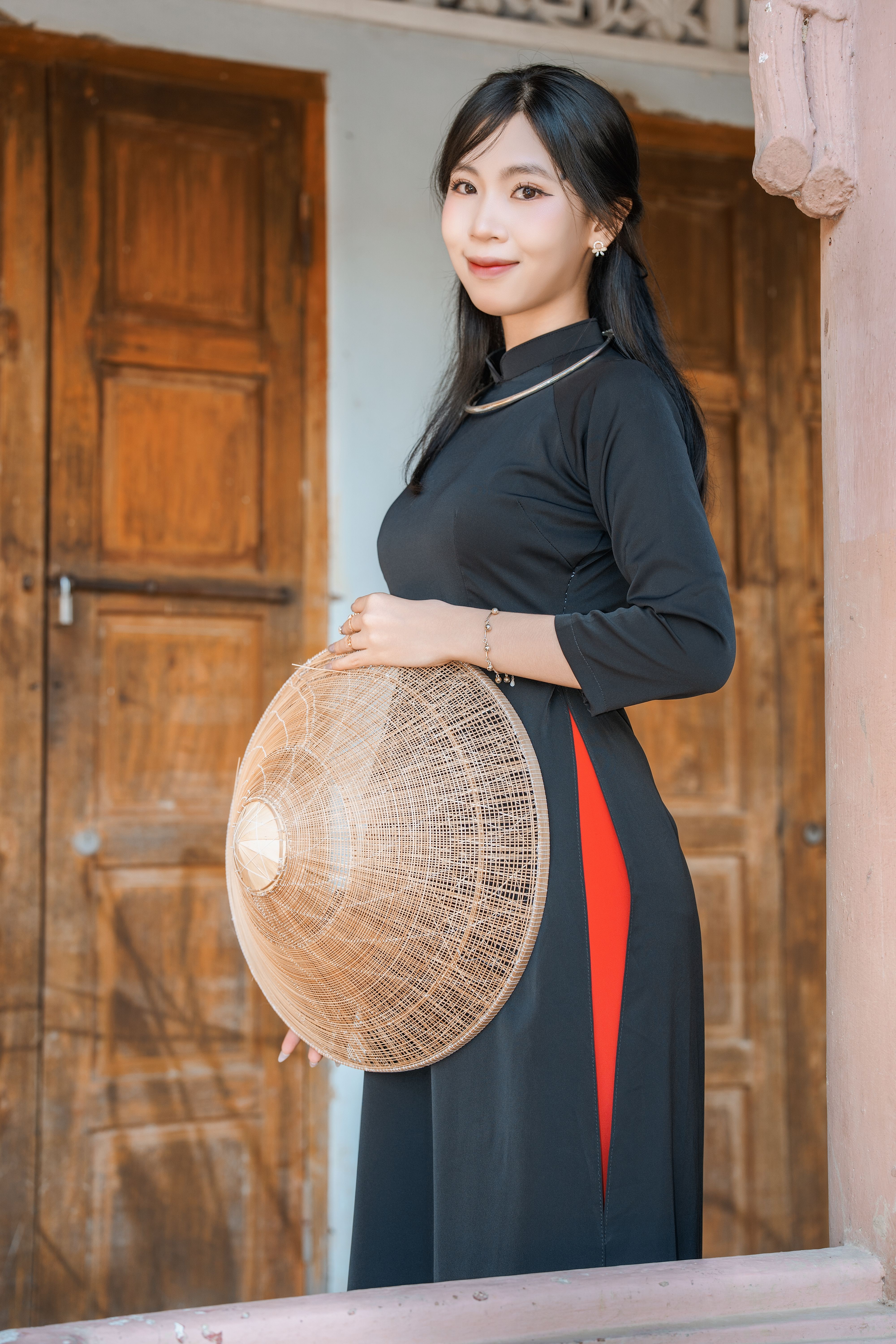 Young woman in traditional attire with a woven hat, standing outdoors against wooden doors.