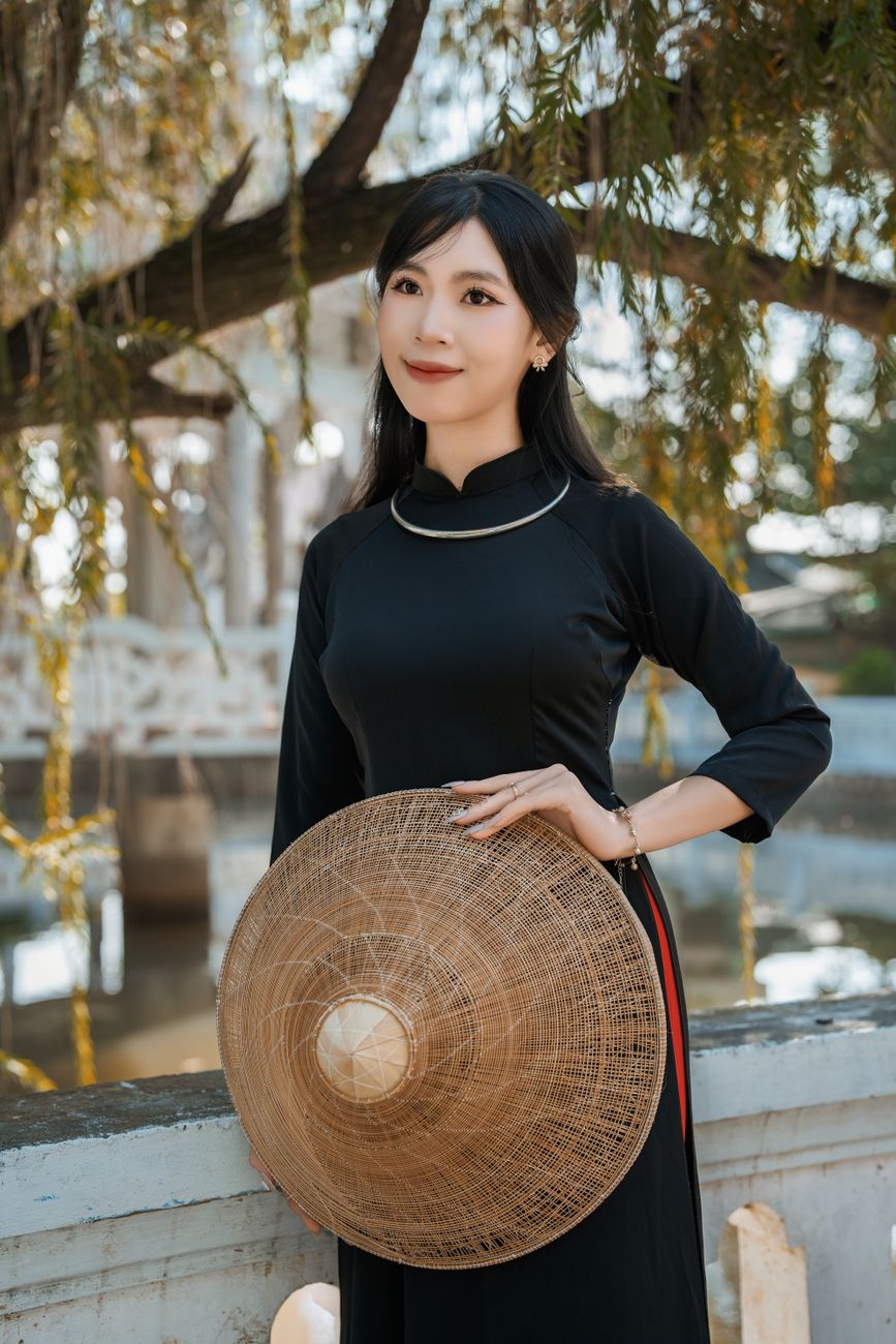 Woman in traditional dress holding hat outdoors, blending culture and nature.