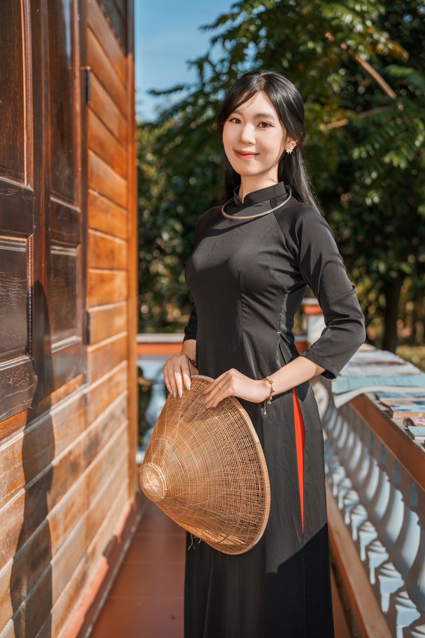 Young woman in traditional Vietnamese ao dai holding a non la outdoors.