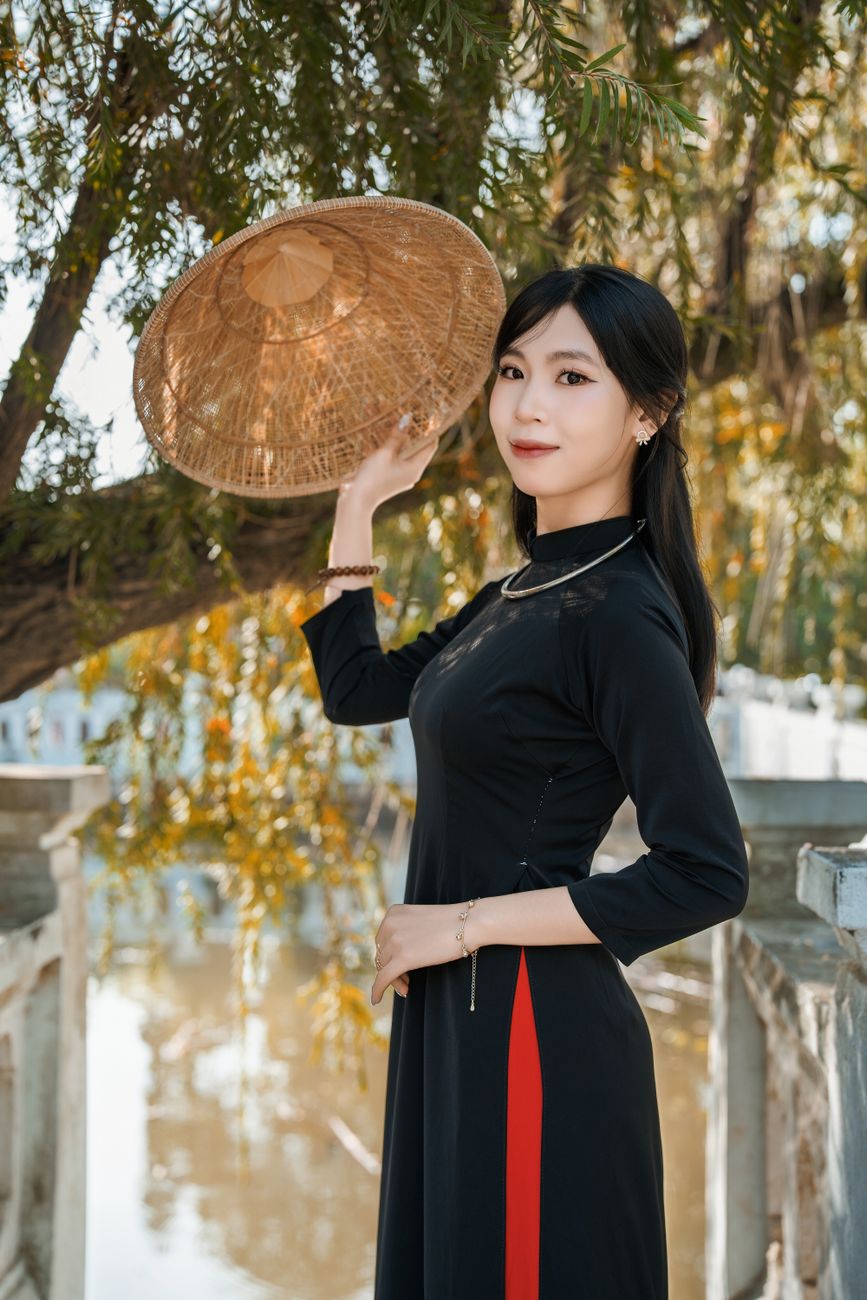 Woman in black traditional dress with straw hat in serene outdoor setting.