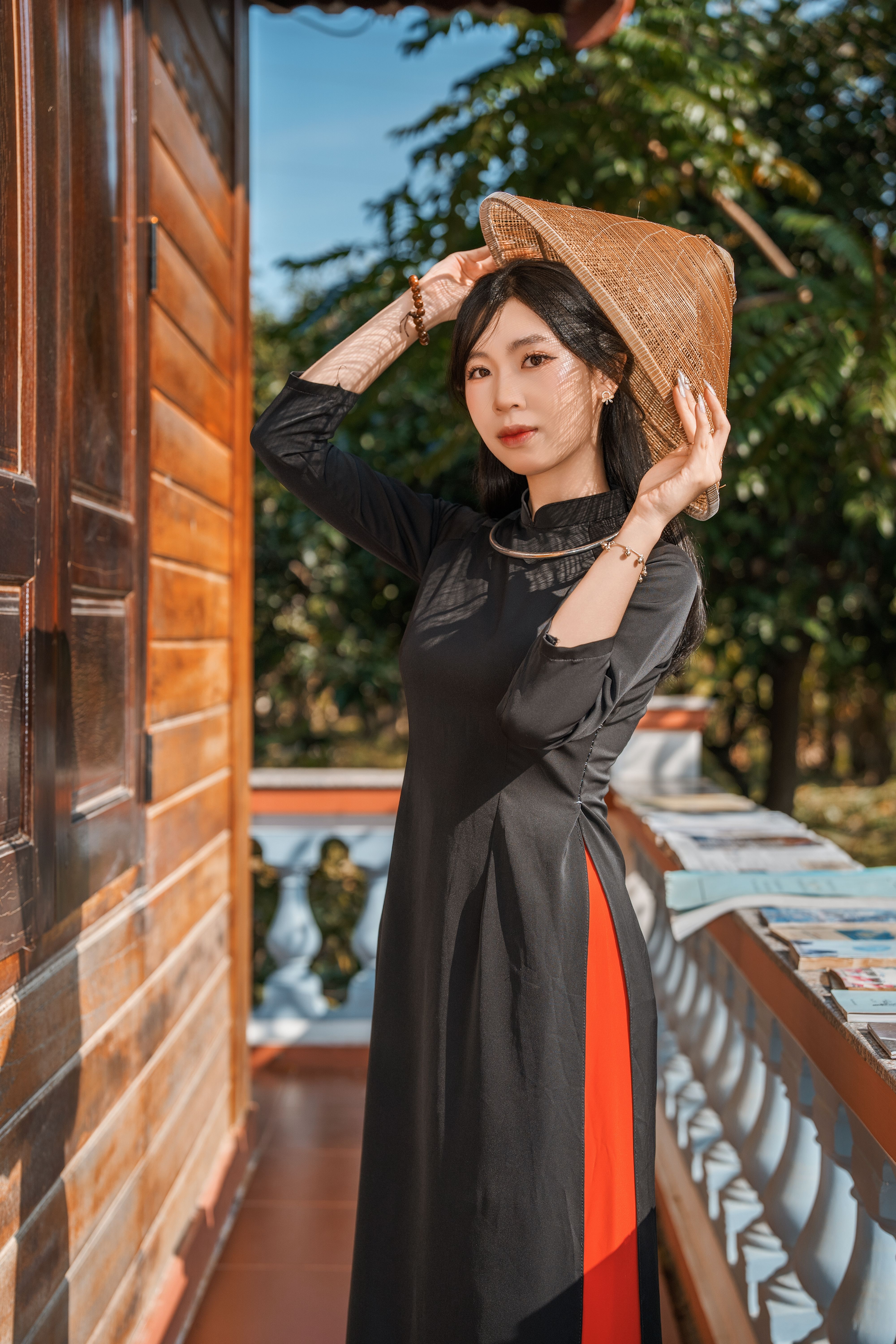 A woman wearing a traditional black dress and conical hat, posing outdoors by a wooden structure.