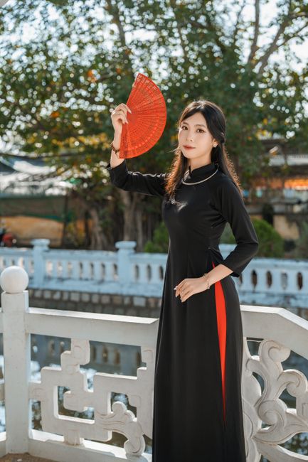 Asian woman in traditional attire gracefully holding a vibrant red fan outdoors, exuding elegance and cultural richness.