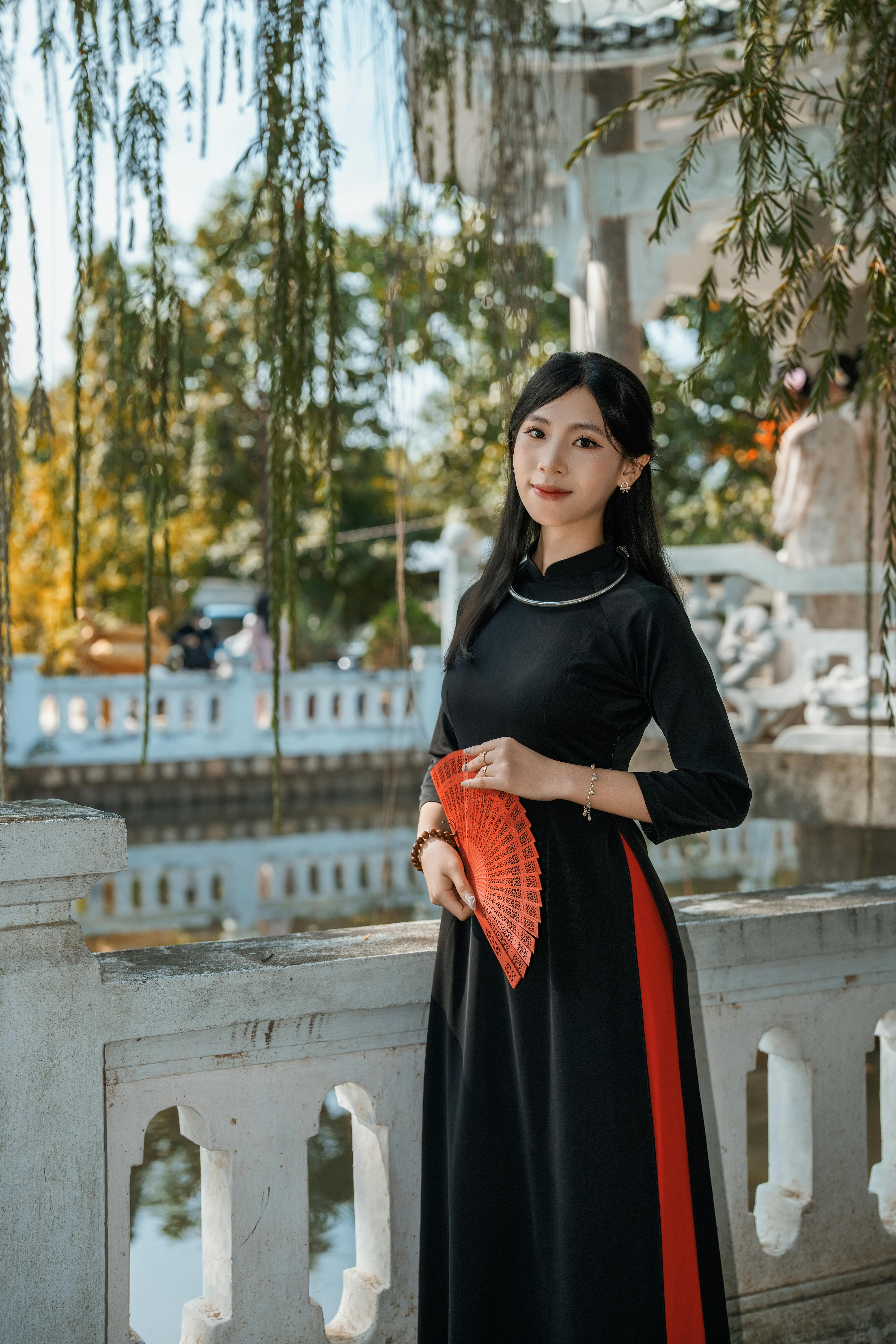 Elegant woman holding a red fan in a serene outdoor setting with traditional architecture.