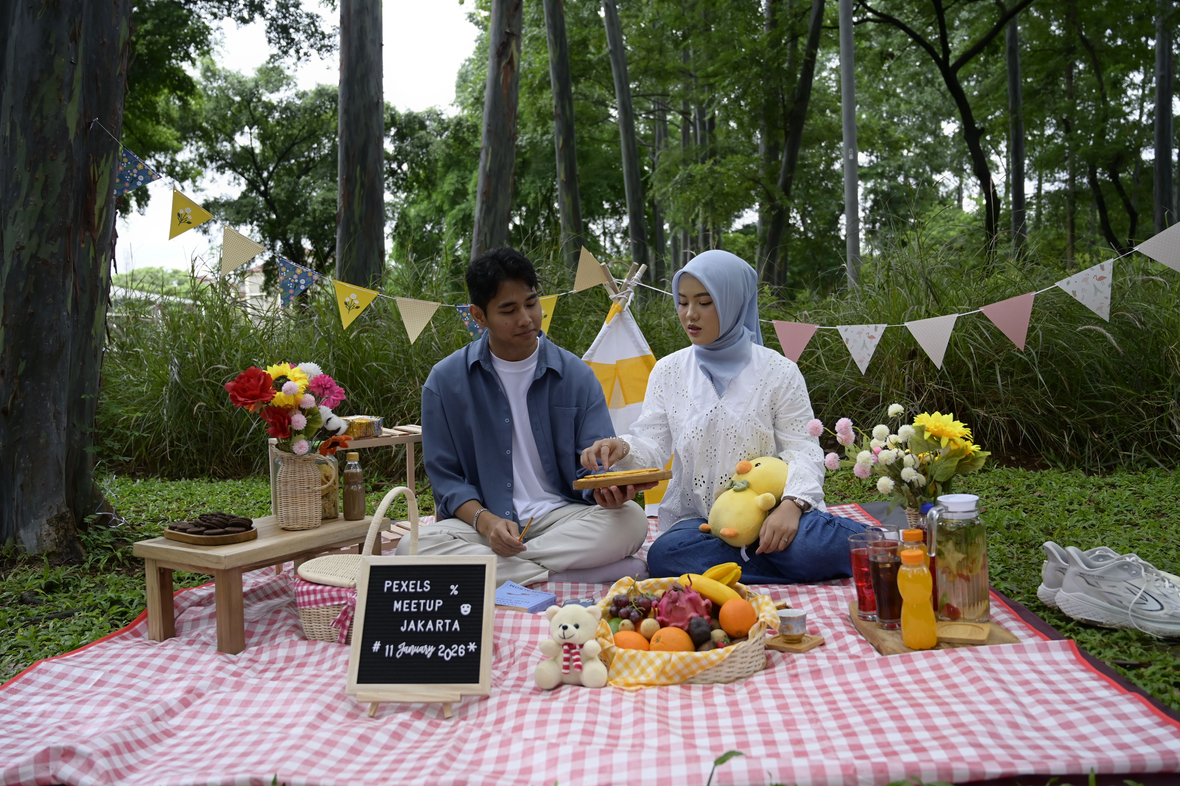 Young couple enjoying a picnic with fruits and drinks in a Jakarta park.