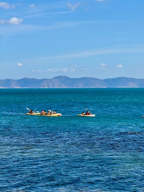Free Kayakers paddle across the ocean with distant mountains under a clear sky. Stock Photo