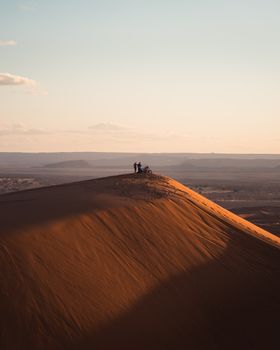 Silhouettes atop a massive sand dune in the Sahara at sunset, capturing serene desert landscape.