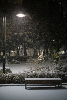 Peaceful park bench under a streetlamp during a snowy winter night, creating a tranquil atmosphere.