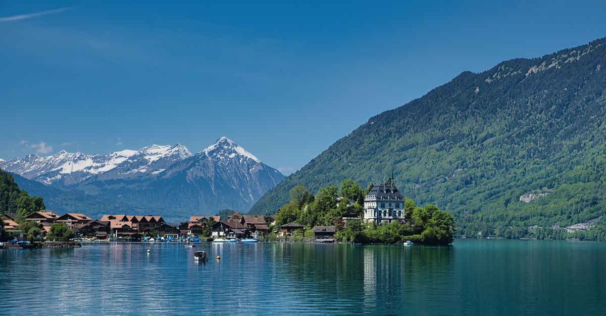 Vue pittoresque d'un charmant village au bord d'un lac, avec des montagnes enneigées et une végétation luxuriante.