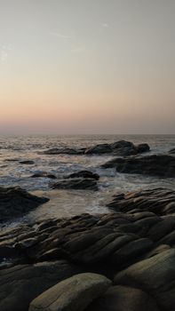 Tranquil sunset view at Ullal Beach, India, with waves crashing on rocks.