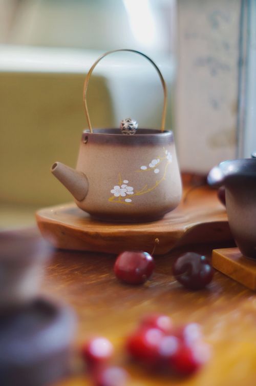 Free Close-up of a ceramic teapot with cherry blossom design and fresh cherries. Stock Photo