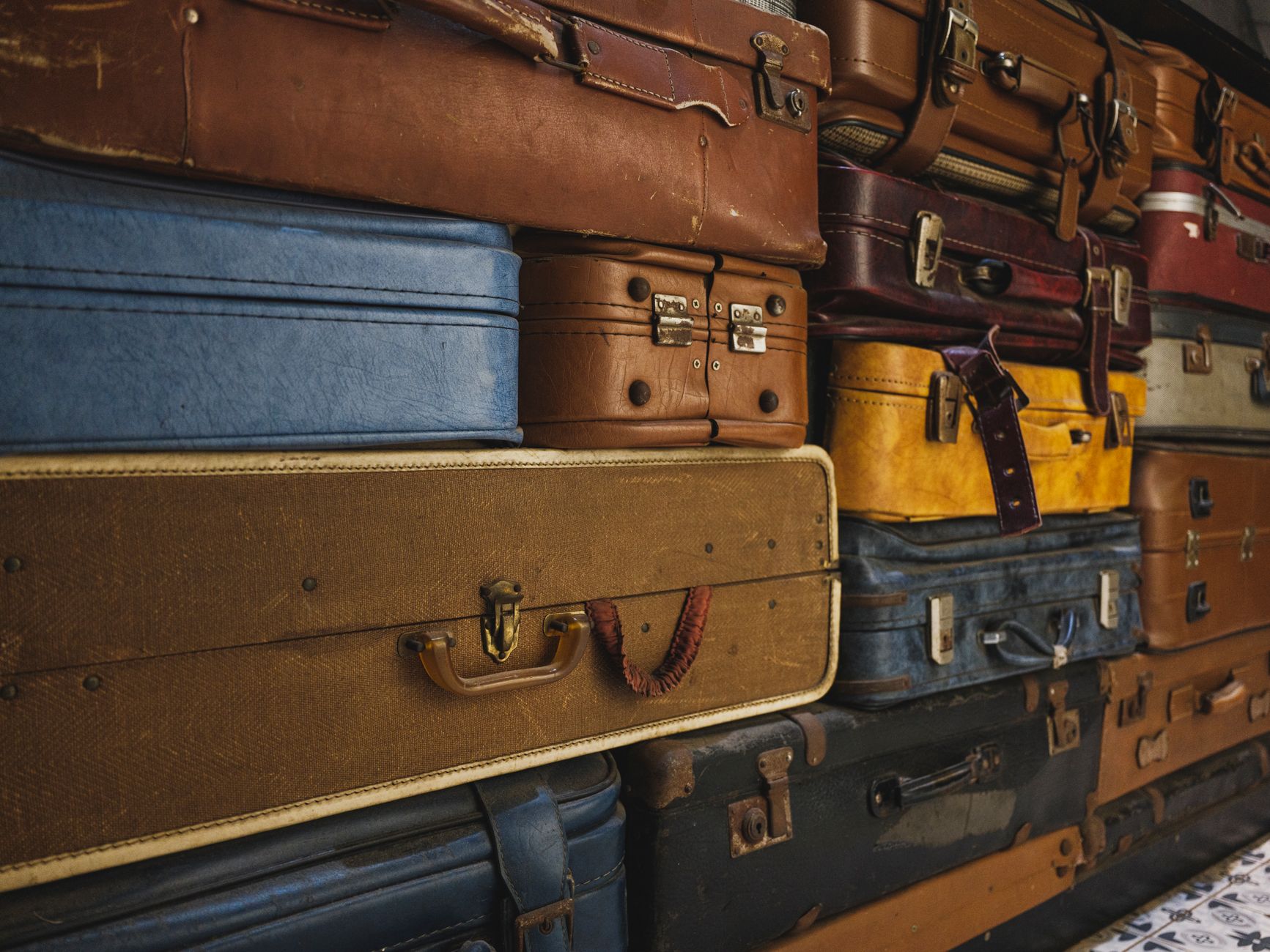 A collection of colorful, worn vintage suitcases stacked together, ideal for decor or travel themes.
