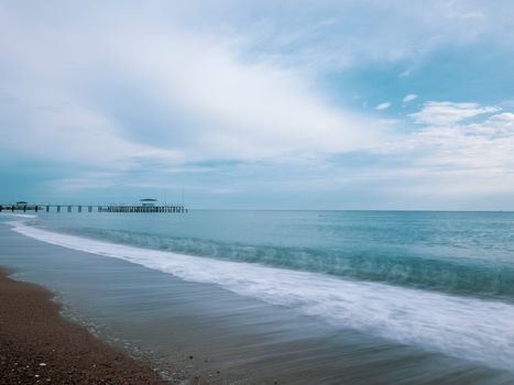 A tranquil ocean scene with soft waves, sandy shore, and a distant pier under a calm sky.