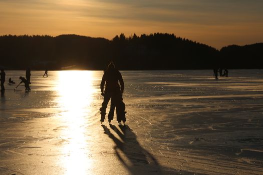 Silhouettes of people ice skating on a frozen lake in Trøndelag, Norway during sunset.