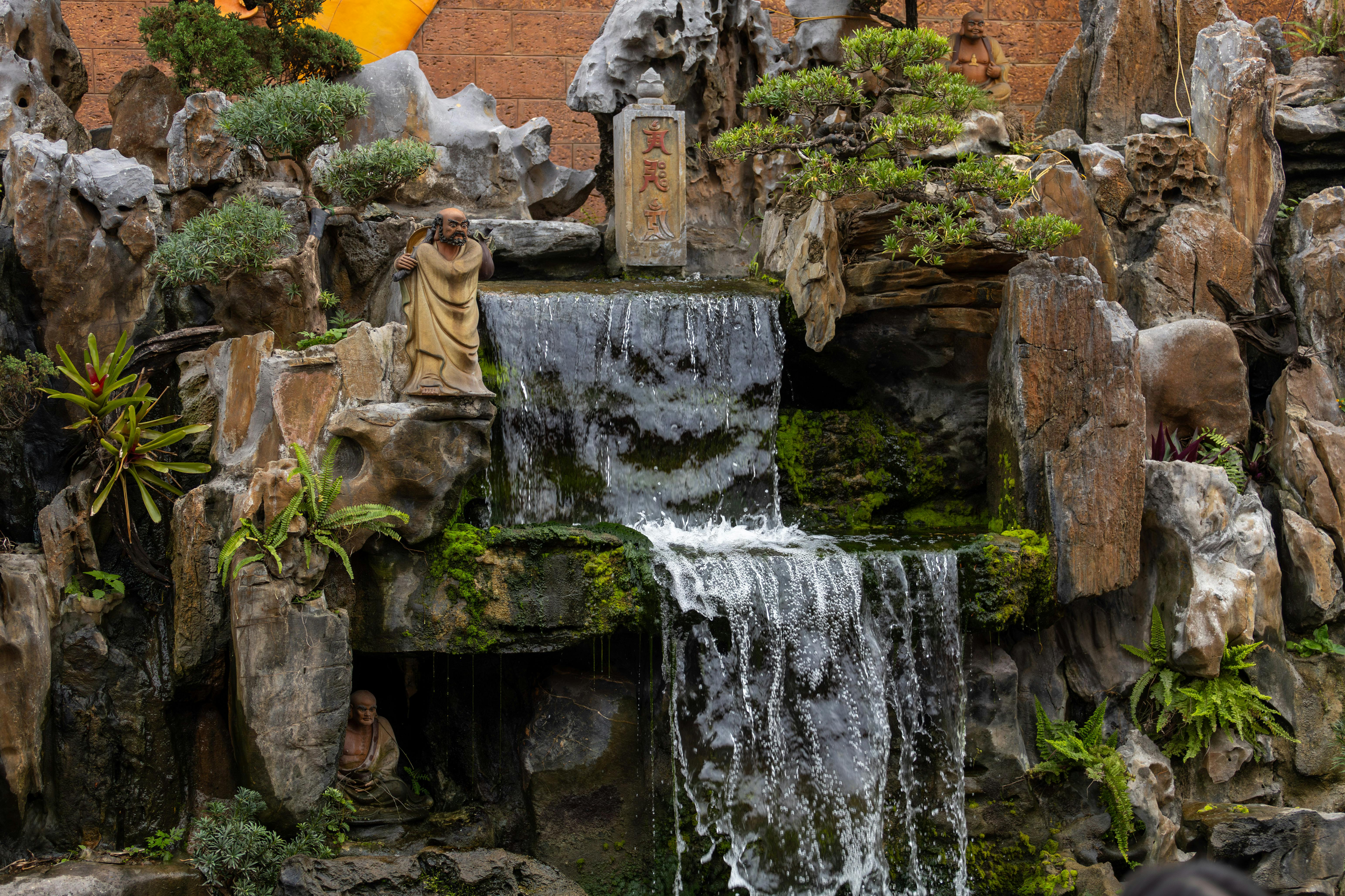 Serene Buddhist statues set against a cascading waterfall in Hanoi, Vietnam.