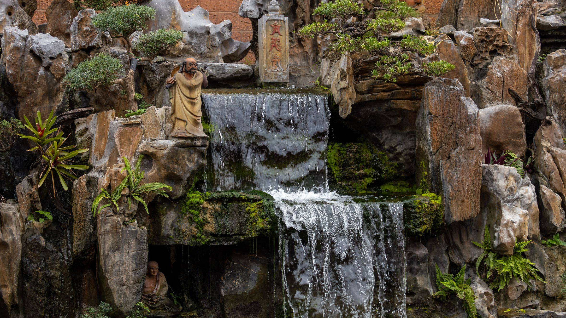 Serene Buddhist statues set against a cascading waterfall in Hanoi, Vietnam.