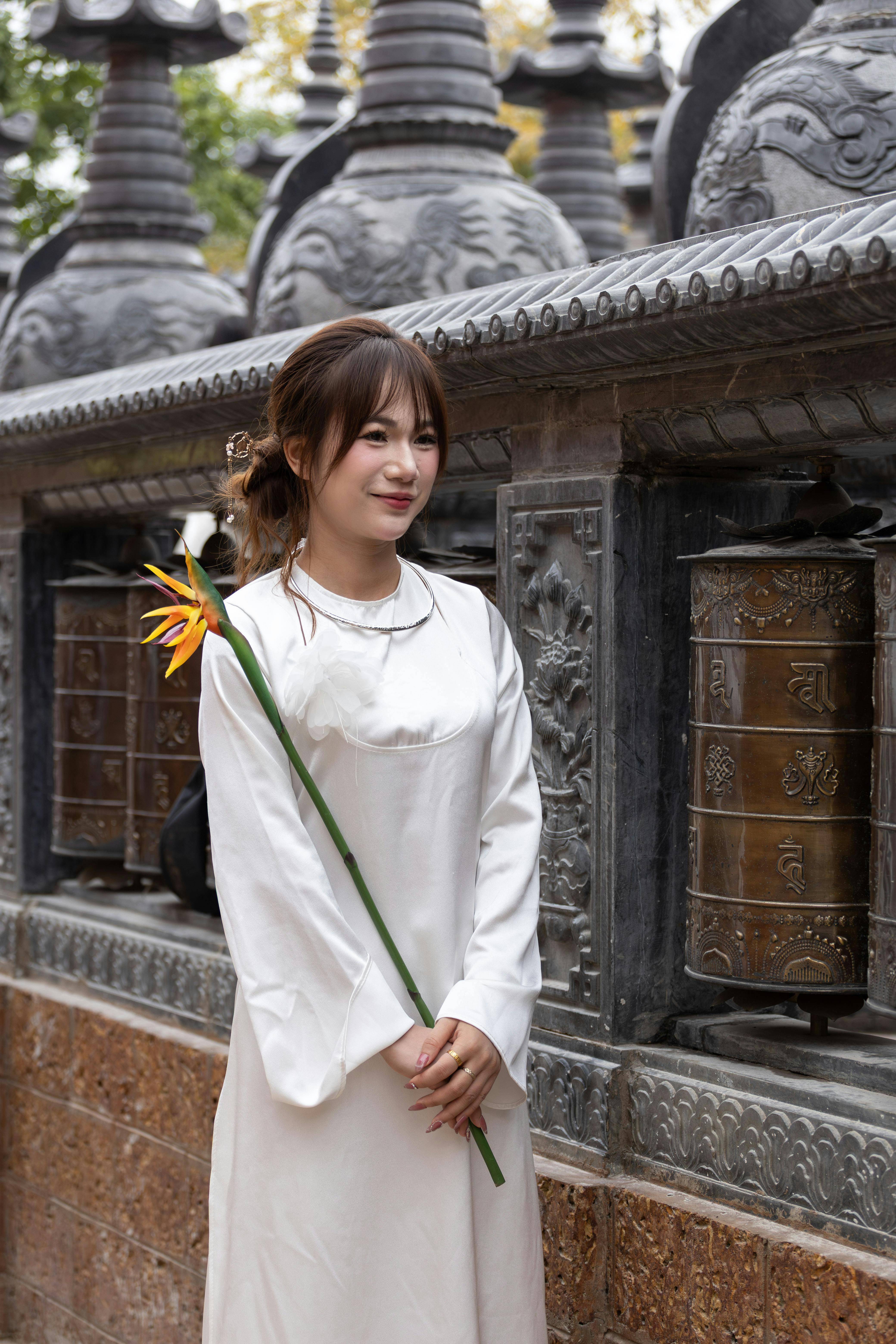 A woman in white traditional dress holds a Bird of Paradise flower at a temple in Hà Nội, Việt Nam.