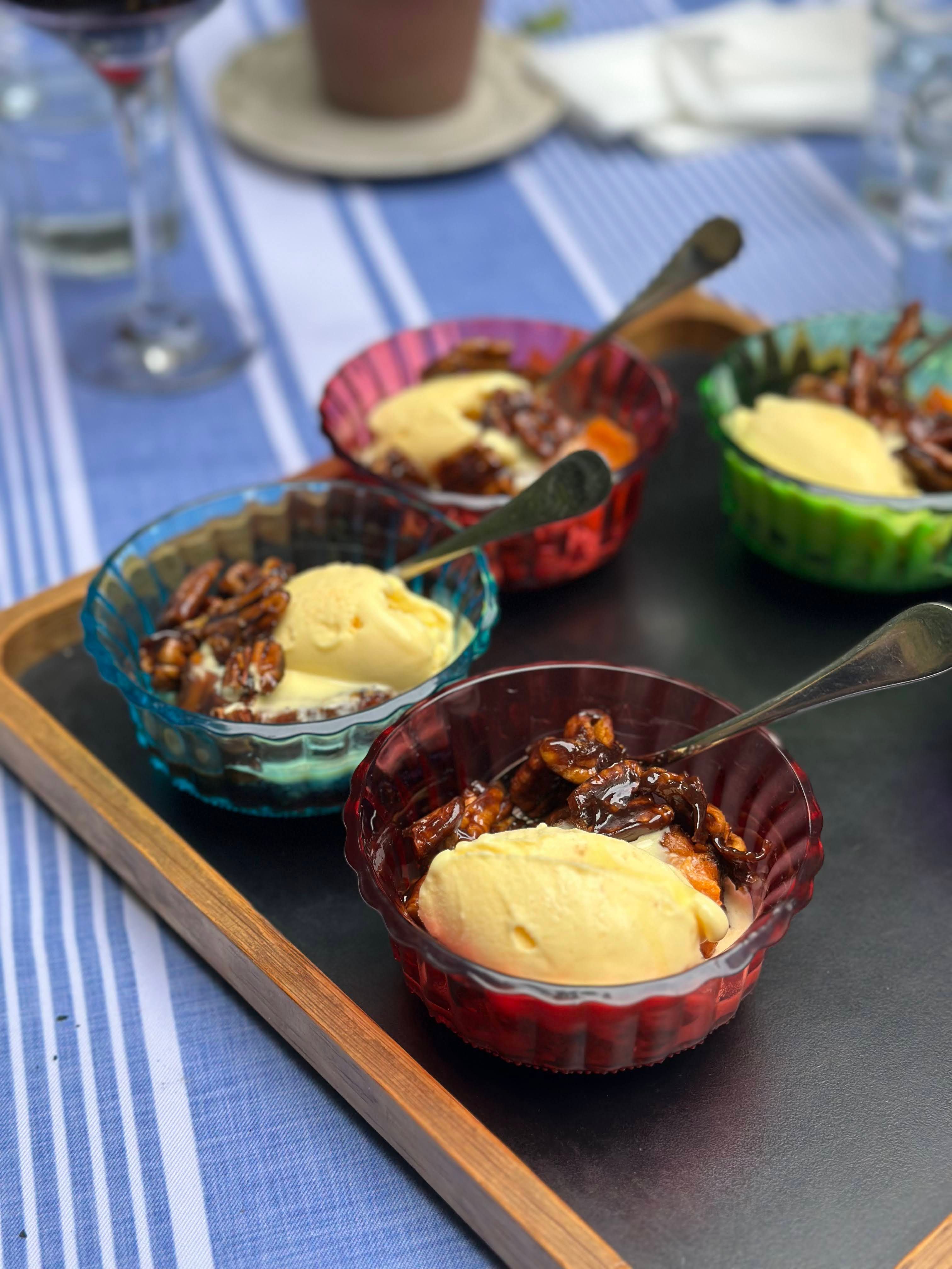 Colorful bowls of vanilla ice cream topped with candied pecans on a tray. Ideal summer dessert.
