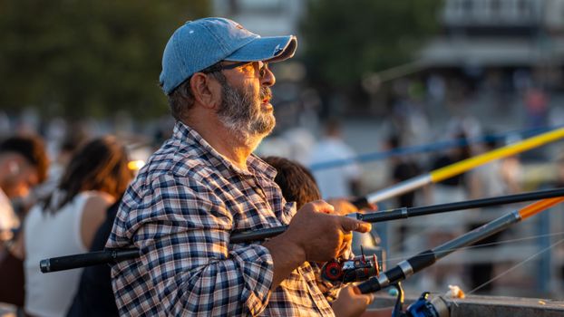 Man fishing outdoors with a focused demeanor during sunset on a busy pier.