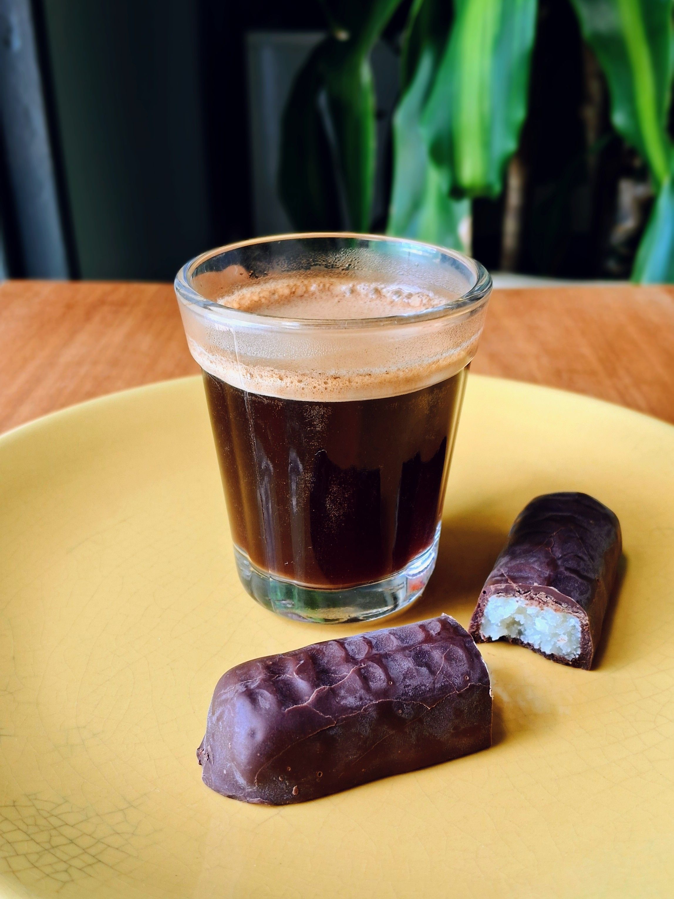 A delicious espresso shot paired with chocolate bars on a yellow plate, perfect for coffee lovers.