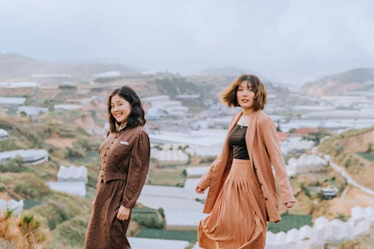 Two women in stylish outfits smiling and posing outdoors with scenic background.