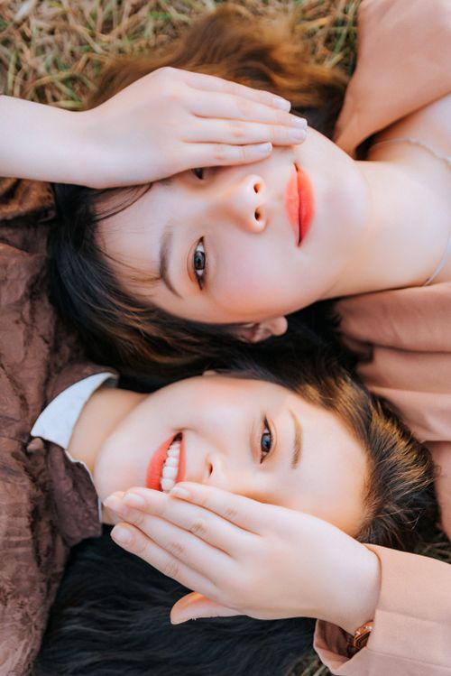 Free Two women with red lips and natural makeup smiling while lying on grass. Stock Photo
