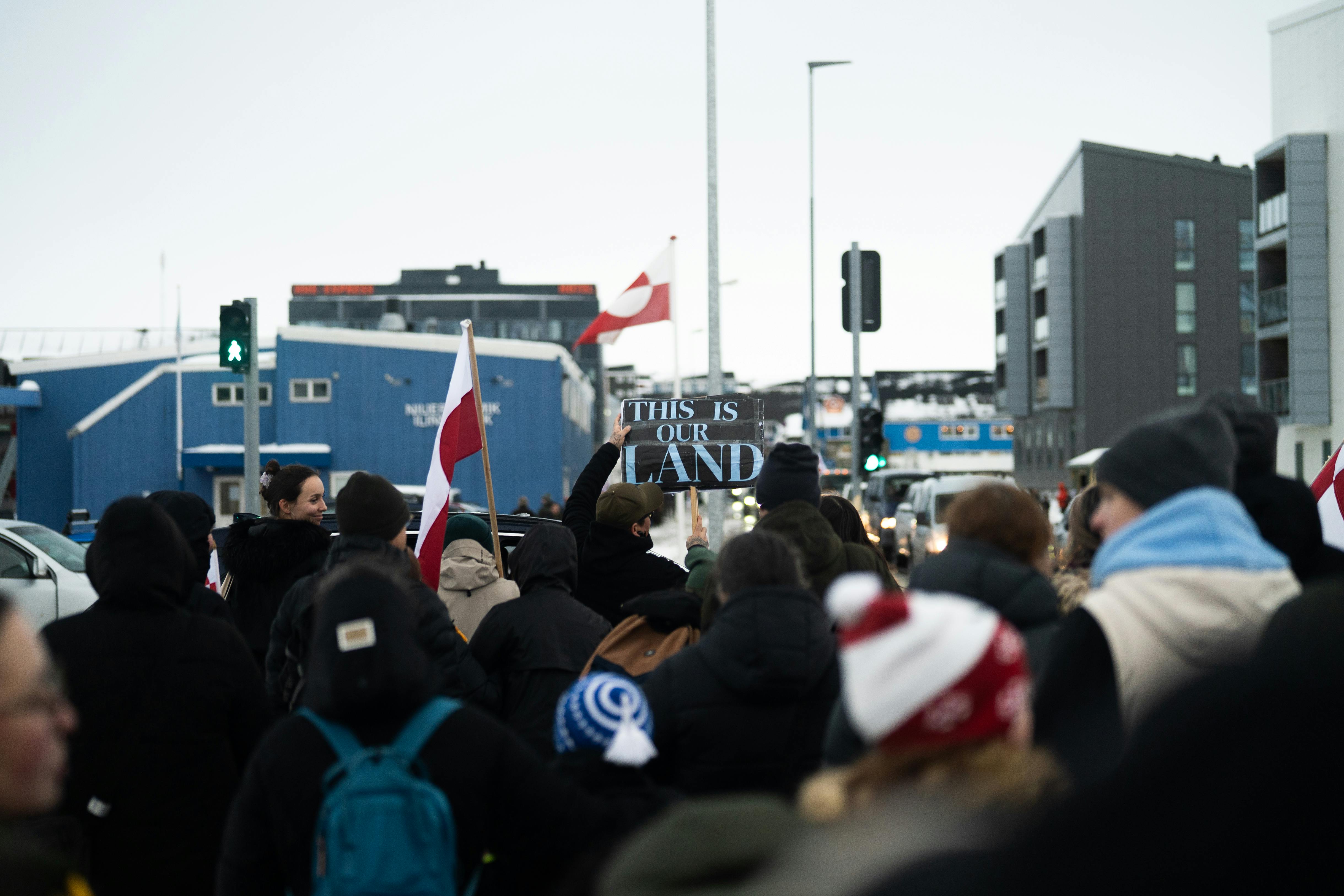 Imajen ida hatudu fabrika produsaun arma iha EUA, iha parte seluk bandeira Greenland no veteranus iha manifestasaun. Hanesan 