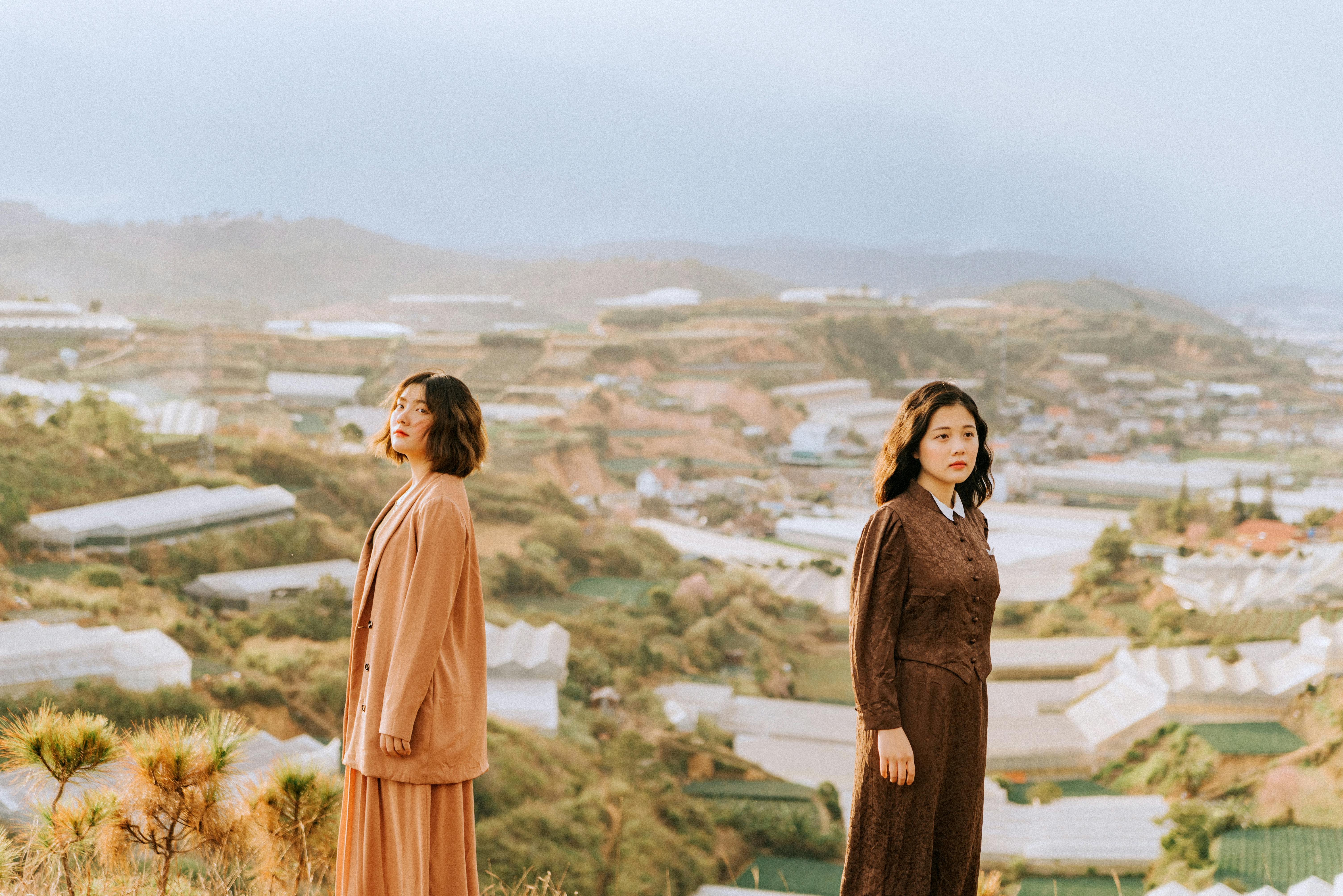 Two stylish women pose in elegant outfits against a beautiful scenic landscape, showcasing autumn fashion.