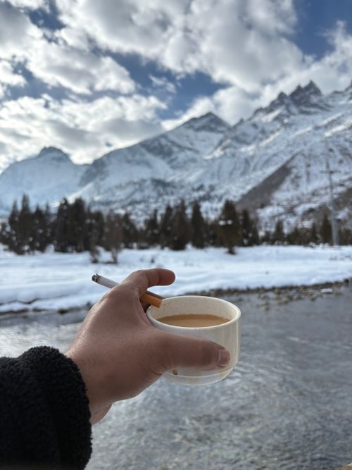 Free Hand holding coffee and cigarette against snowy mountain backdrop. Stock Photo