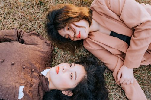 Free Two women with unique hairstyles and fashionable outfits lying on grass, creating a stylish outdoor portrait. Stock Photo