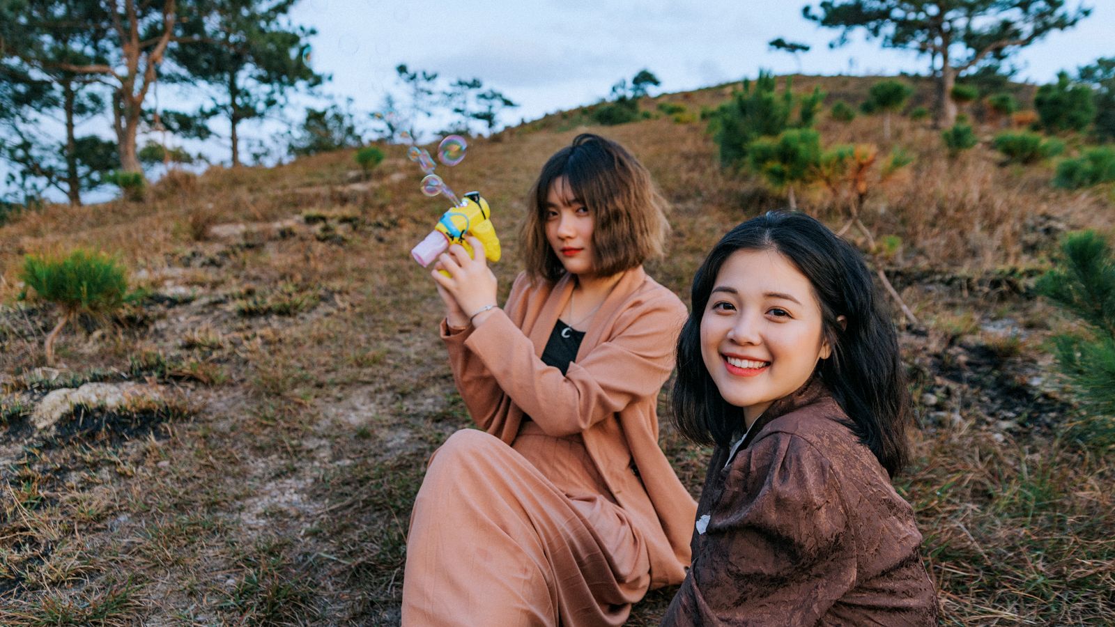 Two people sitting outdoors on grass, one holding a bubble toy