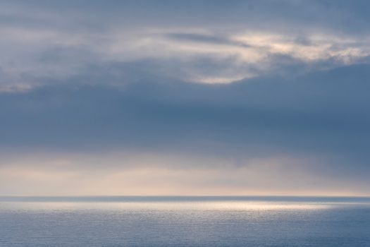 Peaceful seascape with calm waters and dramatic sky at dawn, reflecting serene light.