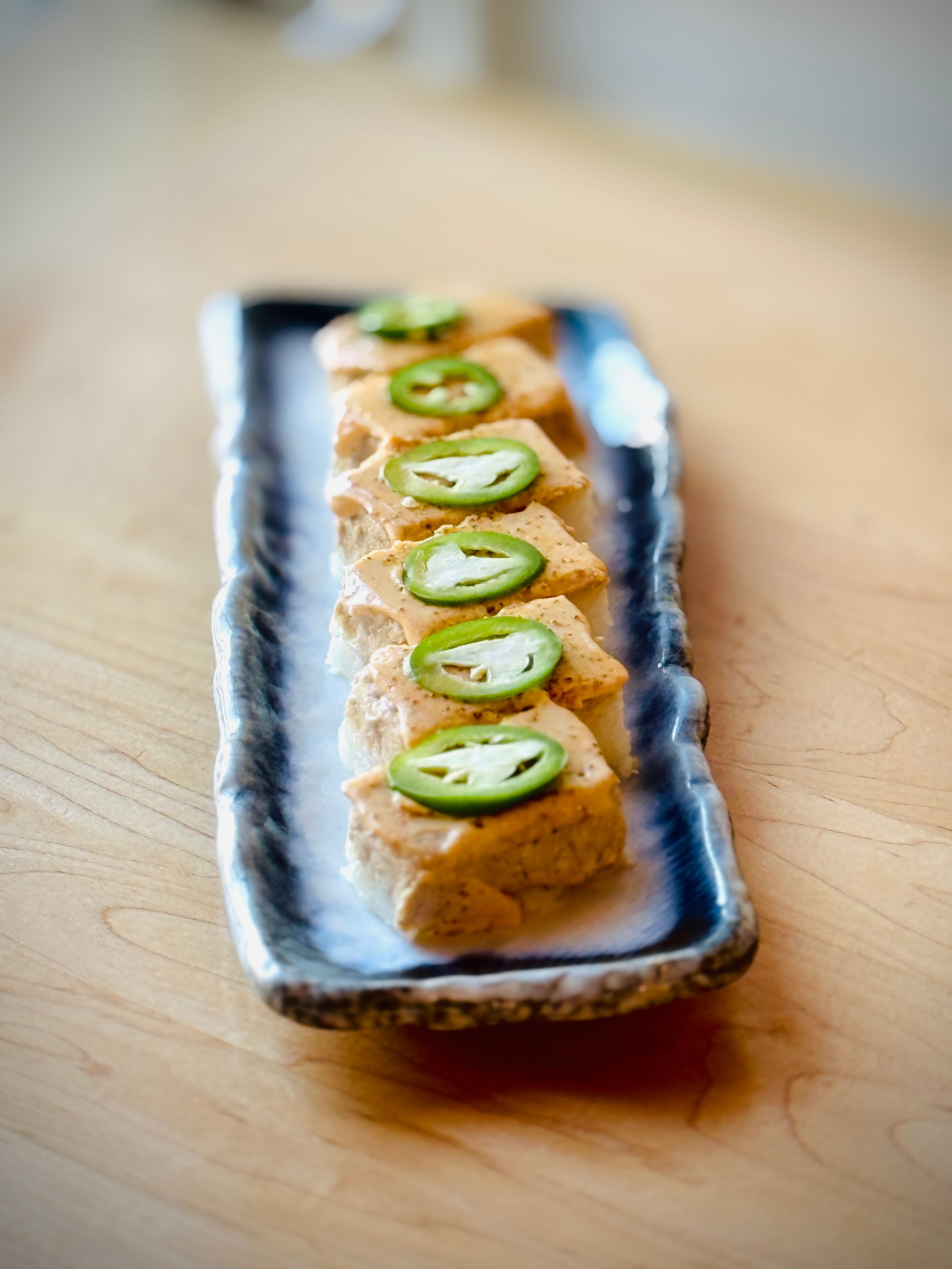 Delicious tofu slices garnished with jalapeno on a stylish ceramic plate, perfect for a gourmet appetizer.