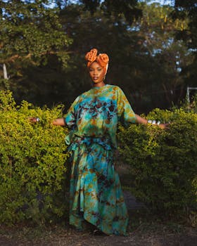 Woman stands confidently in vibrant African print dress and headwrap outdoors.