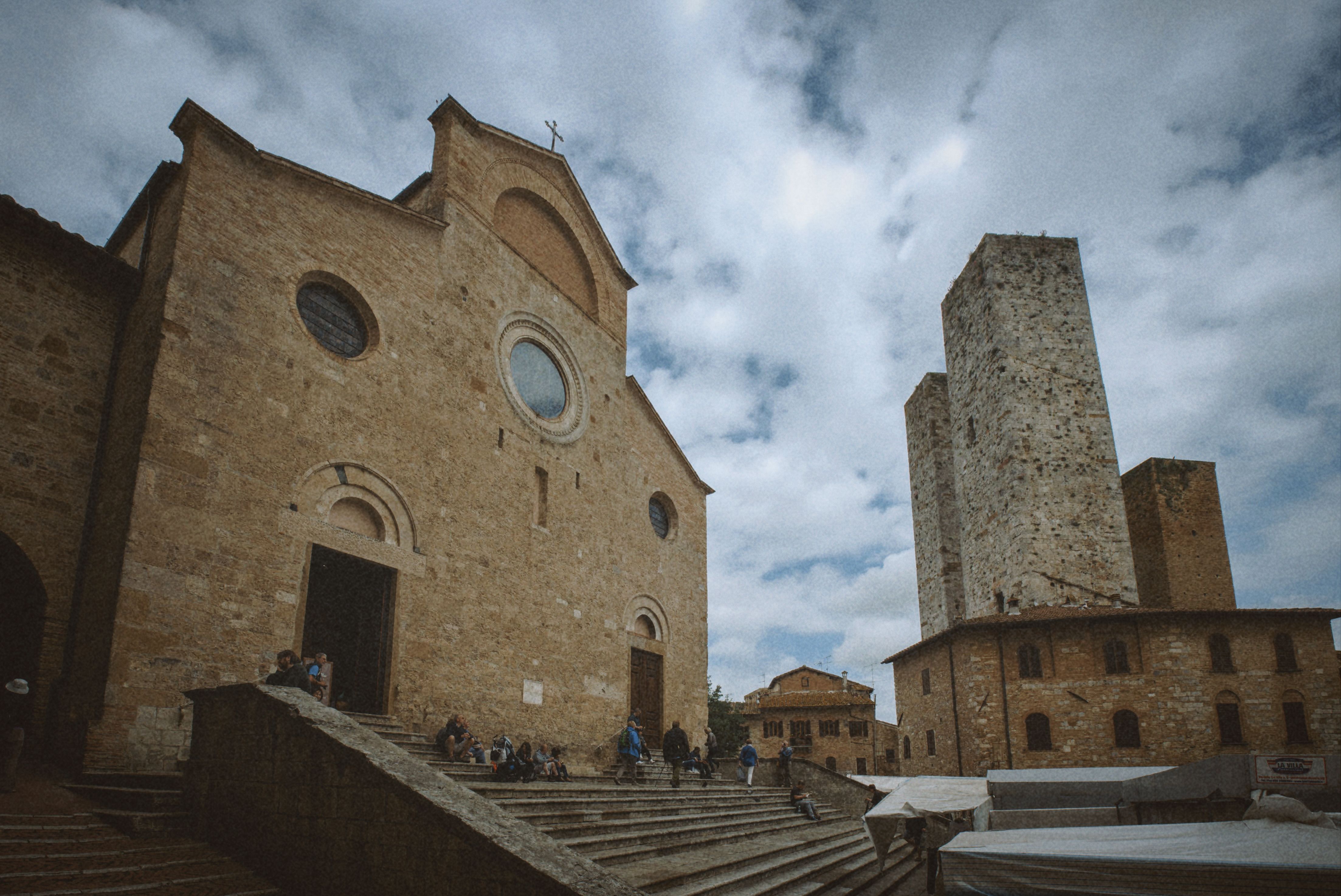 Ancient church with twin towers beneath a cloudy sky in San Gimignano, Italy.