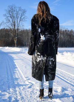 Woman in black coat and blue jeans standing on a snowy road, embracing winter solitude.